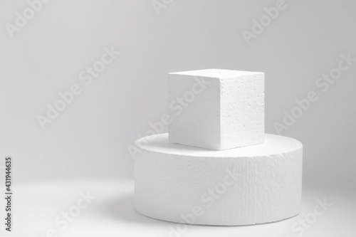 Two white geometric objects made of polystyrene: circle, square, standing one on top of the other on light monochrome background. Concept of an empty 3d podium for presentation of cosmetic products