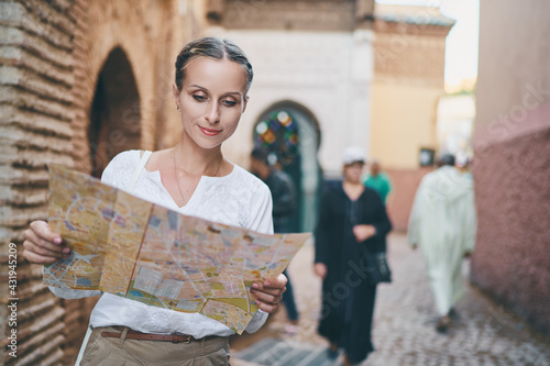 Travel and active lifestyle concept. Young traveller woman walking in ancient moroccan town holding tourist map.
