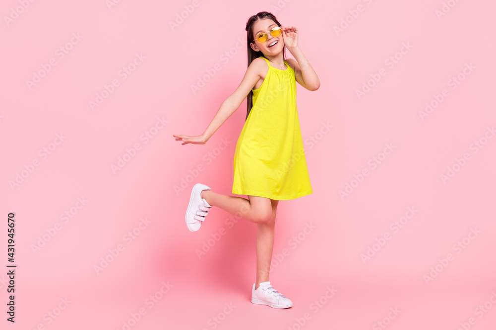 Full length photo of funky charming school girl wear yellow dress dark eyewear smiling dancing isolated pink color background