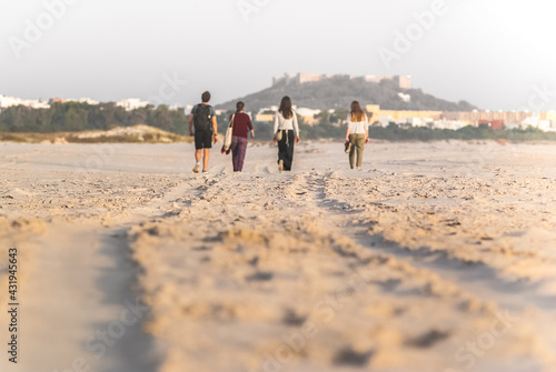 Friends walk on the beach on a sunny day. Back view. Castle and old town in the background.