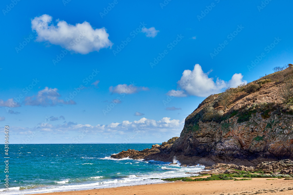 Image of the East section of Geve le Lecq, Jersey CI with sand, rocks, headland and choppy sea in the sunshine with some cloud