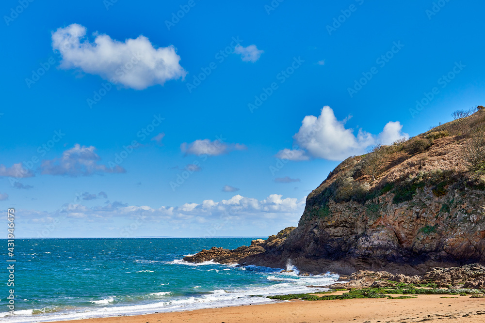 Image of the East section of Geve le Lecq, Jersey CI with sand, rocks, headland and choppy sea in the sunshine with some cloud Image of the East section of Geve le Lecq, Jersey CI with sand, rocks, headland and choppy sea in the sunshine with some cloud