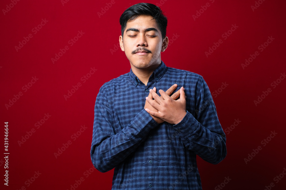 Handsome young man wearing casual clothes smiling with hands on chest with closed eyes and grateful gesture on face Handsome young man wearing casual clothes smiling with hands on chest with closed eyes and grateful gesture on face