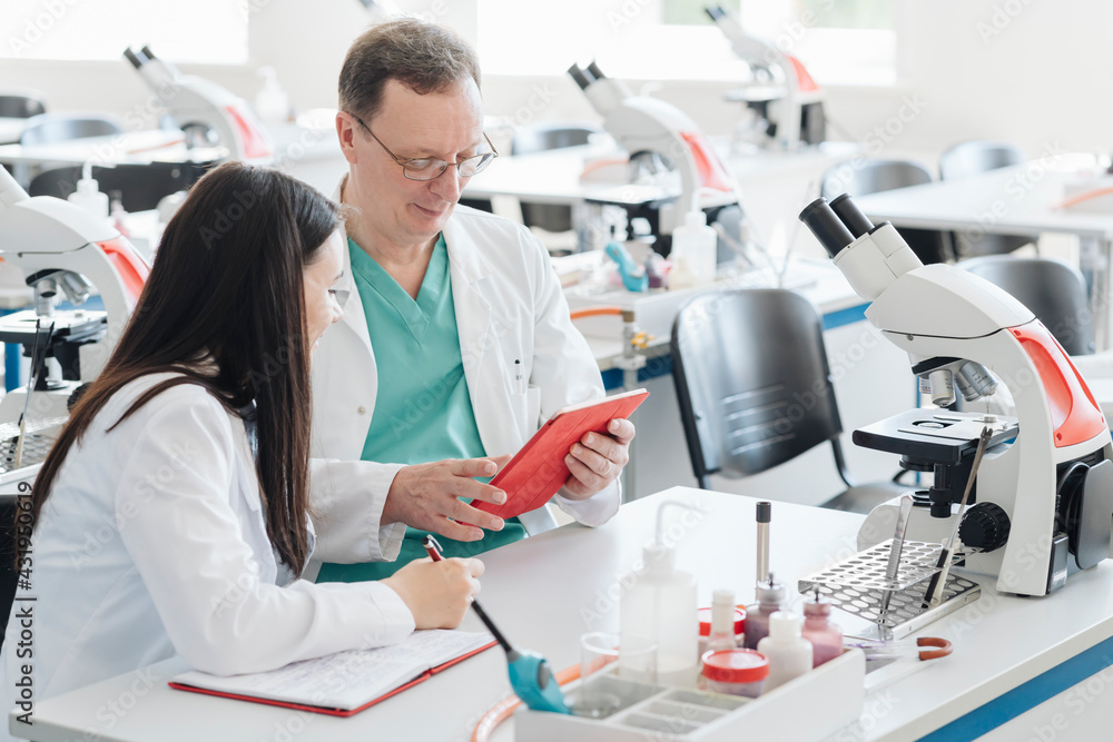 Scientists in white coats using tablet in lab Scientists in white coats using tablet in lab