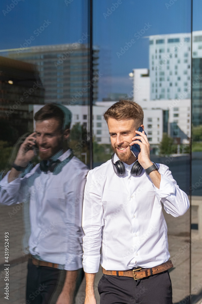 Businessman talking on mobile phone while leaning on glass wall Businessman talking on mobile phone while leaning on glass wall