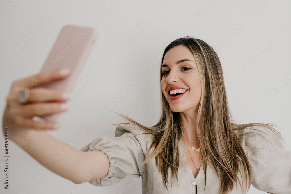 Smiling beautiful woman taking selfie through smart phone against white background Smiling beautiful woman taking selfie through smart phone against white background