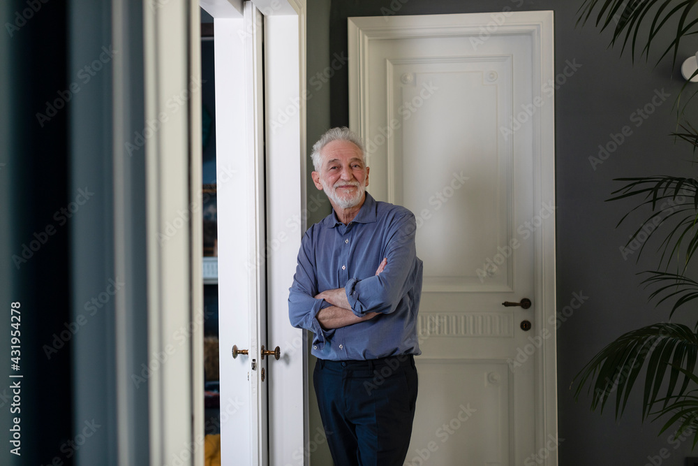 Senior man with arms crossed leaning on wall at home Senior man with arms crossed leaning on wall at home