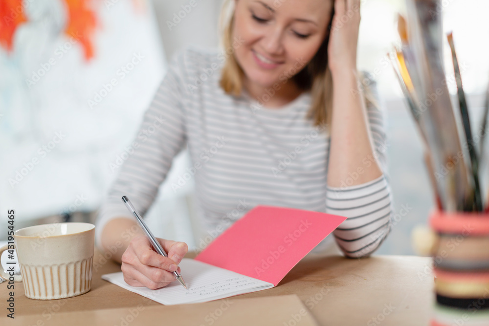 Smiling woman with coffee cup writing in book on table while sitting at home studio Smiling woman with coffee cup writing in book on table while sitting at home studio