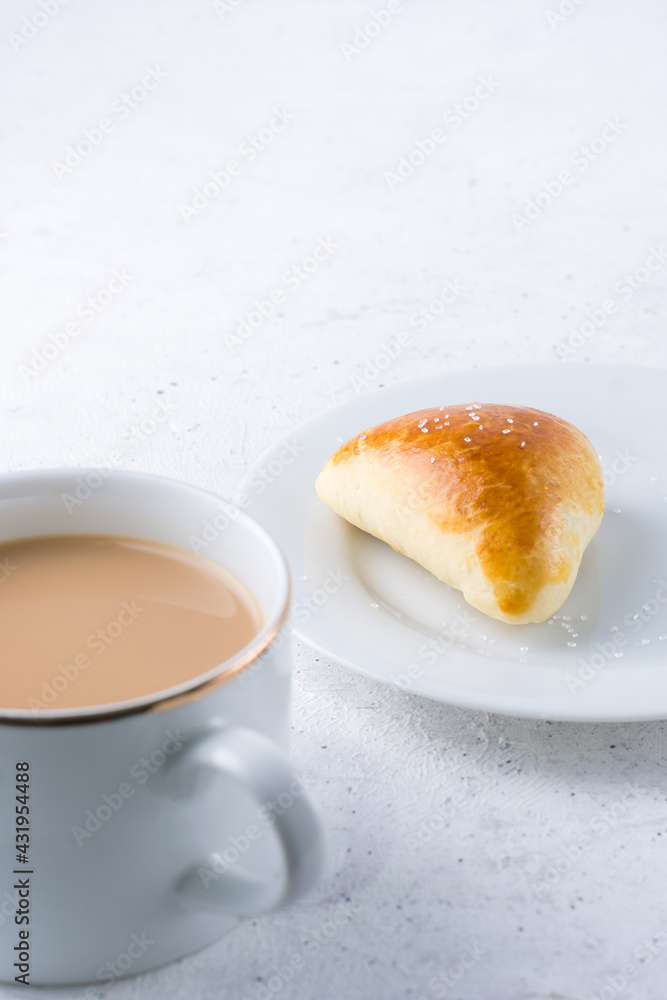 sugar bun and cup of milk tea on white textured background