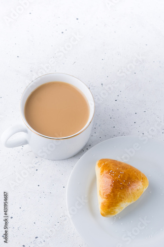 sugar bun and cup of milk tea on white textured background, top view