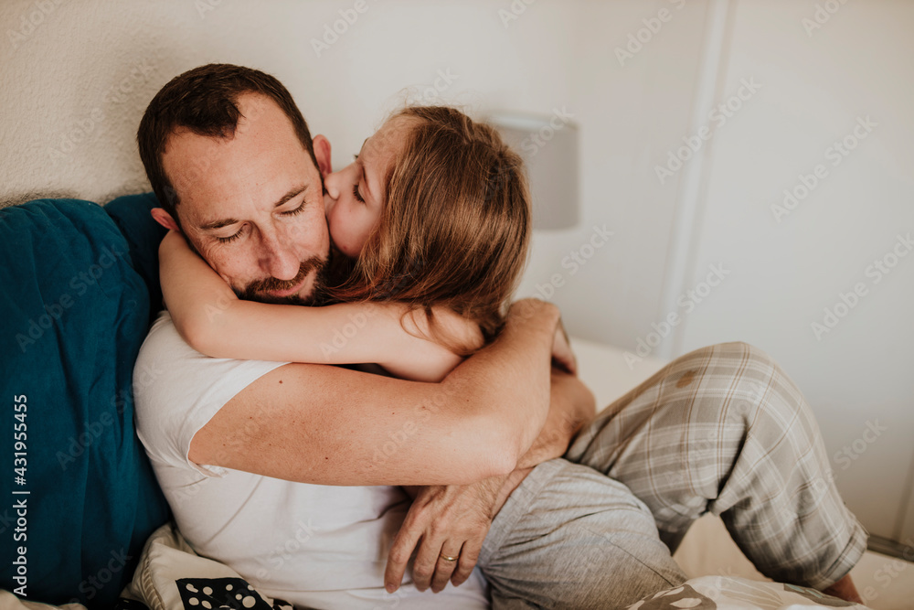 Daughter kissing father on cheek while hugging on bed at home Daughter kissing father on cheek while hugging on bed at home