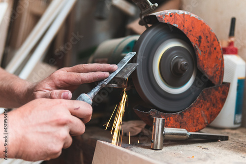 Male carpenter sharpening chisel using grinder in workshop
