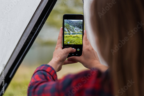 Girl taking photos of the rocky mountains and lake using the phone. Close-up shot of the handі holding the phone. View from the tent.
