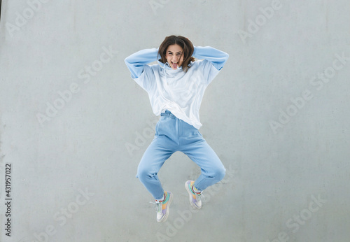 Carefree woman with hands behind head jumping against gray wall photo