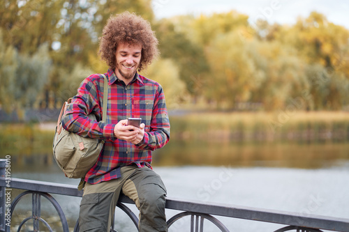 Young handsome man with curly hair using smartphone in ppark. photo