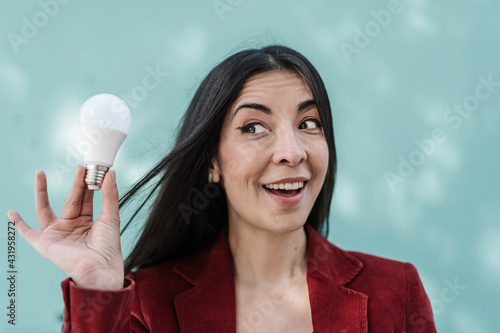 Surprised businesswoman holding light bulb against turquoise wall photo