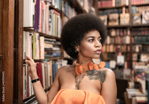 Thoughtful young woman looking away by bookshelf at library