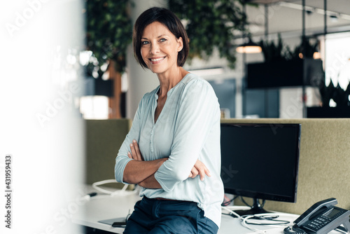 Smiling female entrepreneur with arms crossed against computer in office photo