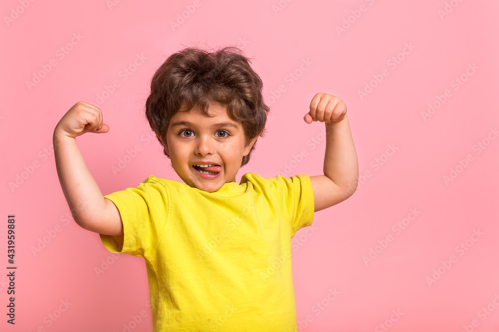 Funny little sportive kid boy in yellow shirt, showing his muscles