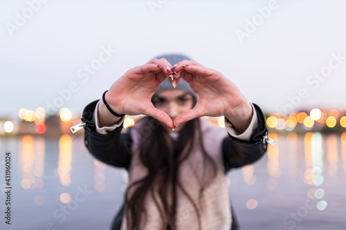 Teenage girl doing heart with her hands during sunset photo