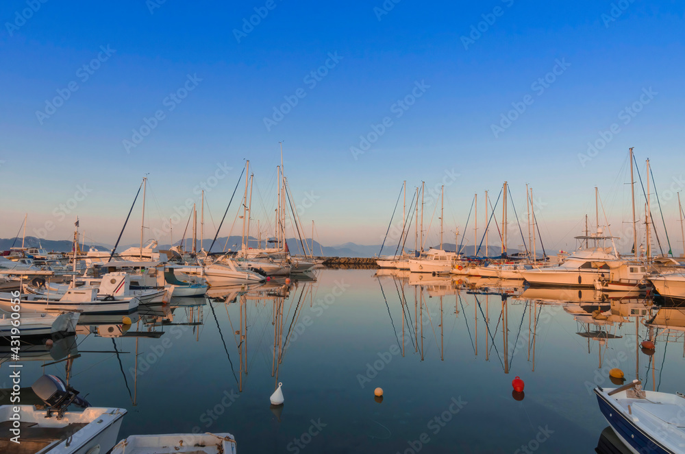 Fototapeta premium Port of charming Aegina town with yachts and sail boats docked in Aegina island, Saronic gulf, Greece, at sunset.