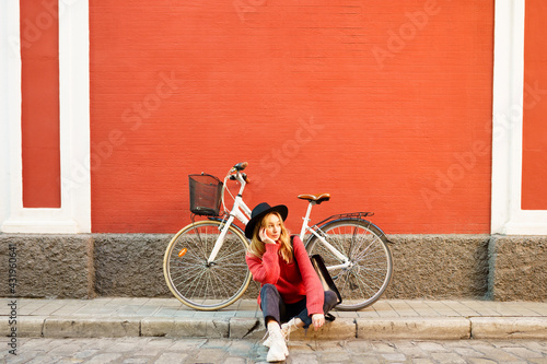 Woman with hand on chin looking away while sitting against bicycle on footpath photo