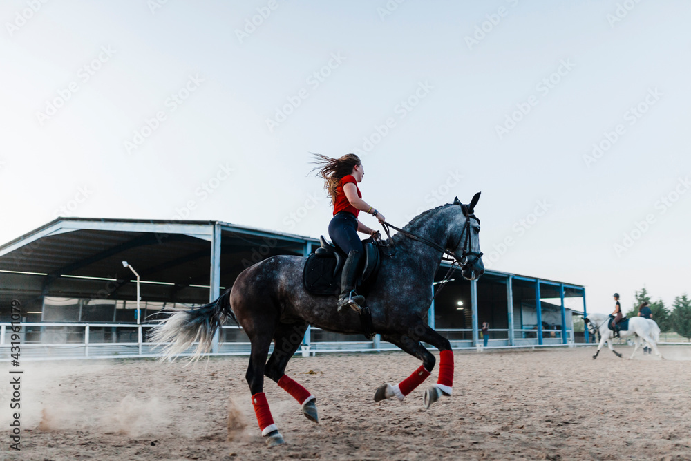 Young woman riding horse in farm during weekend Young woman riding horse in farm during weekend