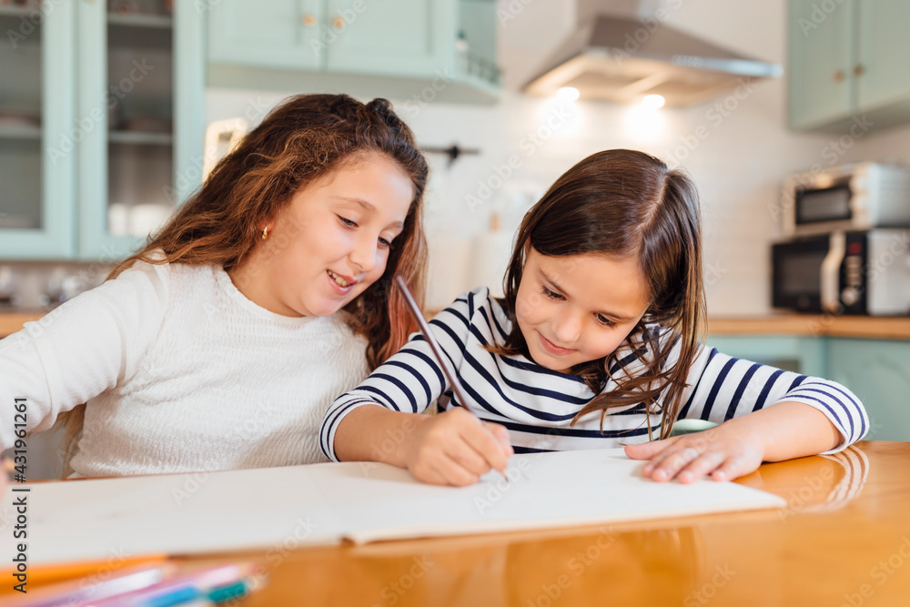 Girl drawing on paper while sitting by sister at dining table in kitchen Girl drawing on paper while sitting by sister at dining table in kitchen