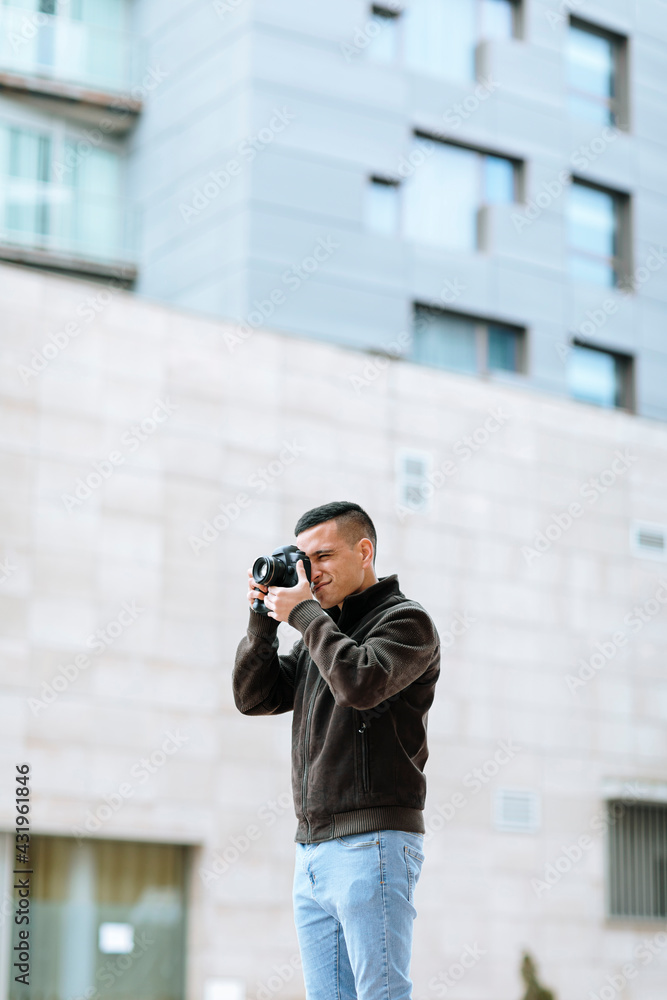 Young male professional photographing through camera while standing against building Young male professional photographing through camera while standing against building