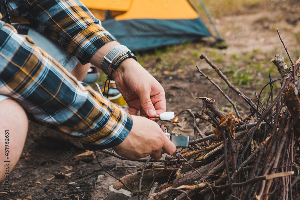 Obraz premium young strong man light a fire at camping site yellow tent on background