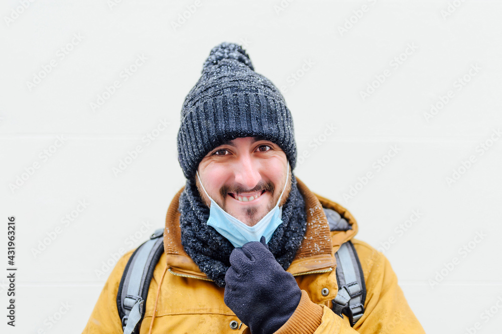 Smiling man pulling mask against white wall during COVID-19 Smiling man pulling mask against white wall during COVID-19