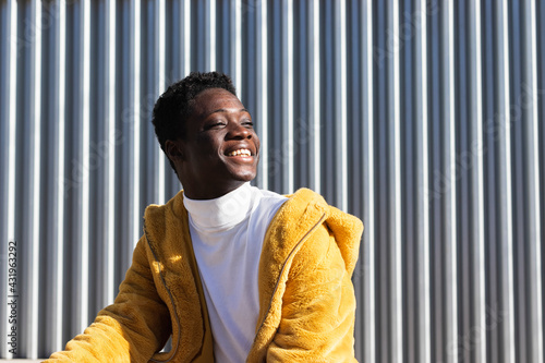 Smiling African man in yellow jacket against white wall looking away 