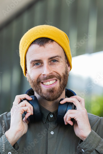 Smiling man holding headphones around neck against building photo