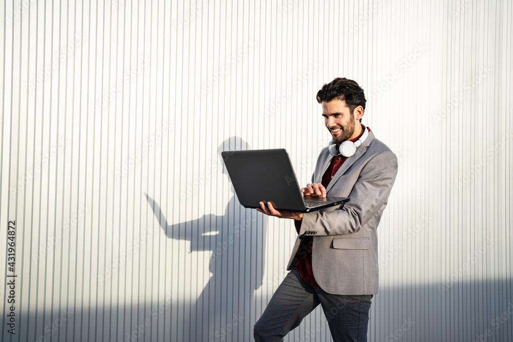 Smiling businessman using laptop in front of wall