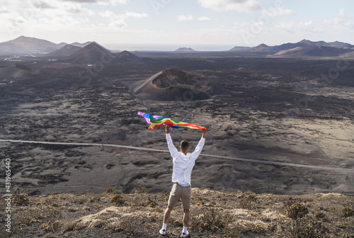 Young male tourist waving rainbow flay while standing at El Cuervo Volcano during vacations, Lanzarote, Spain photo