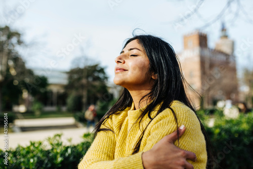 Smiling woman hugging self against sky in public park photo
