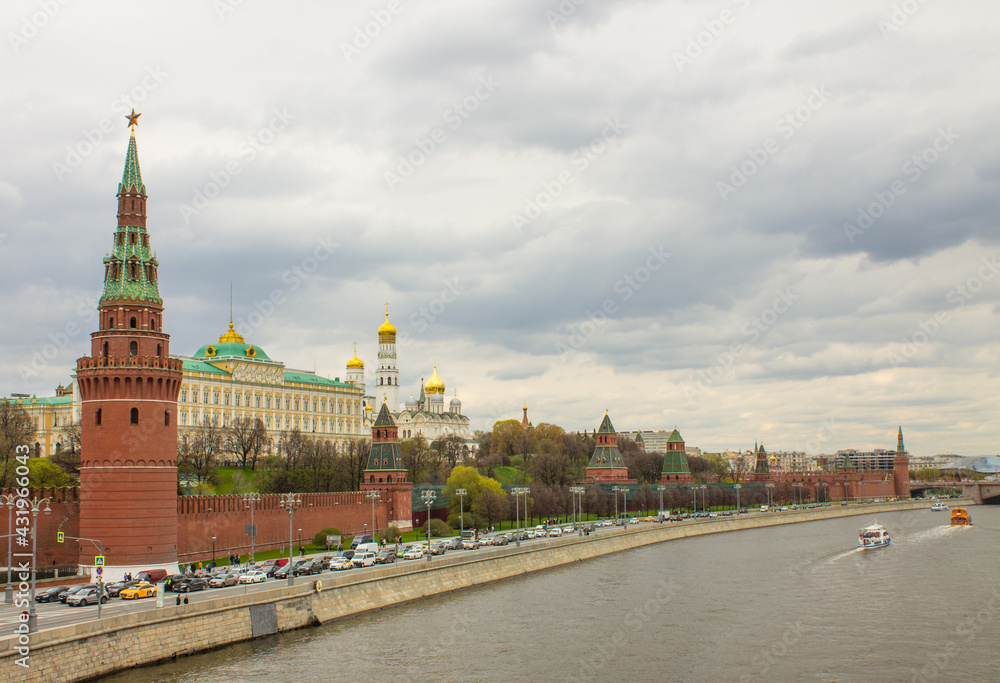 Moscow / Russia - May, 5, 2021: view of the brick wall, the yellow Grand Kremlin Palace and the Assumption Cathedral with golden domes on the banks of the Moskva River on a cloudy spring day