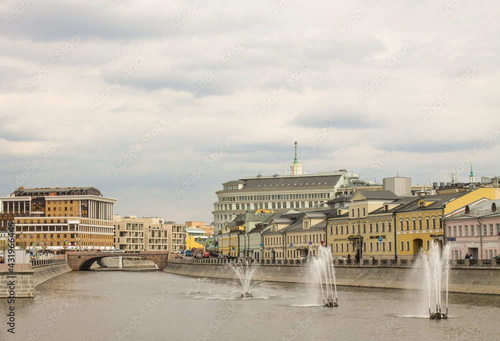 Naklejka premium panoramic view of the Kadashevskaya embankment of the Drainage Canal with beautiful water fountains and historical architecture against the background of a cloudy sky in Moscow