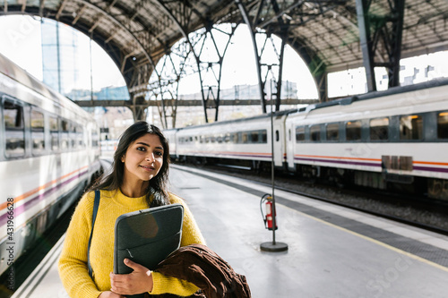 Mid adult woman with laptop bag looking away while standing on railroad station platform
