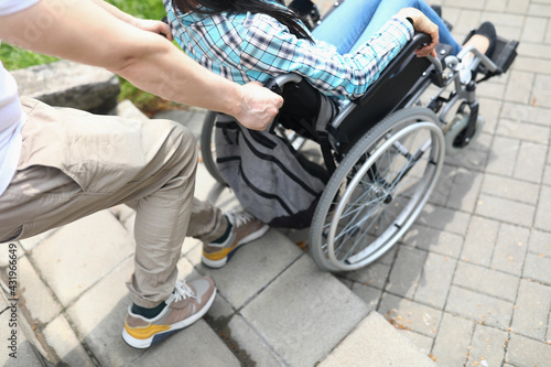 Man lifts a woman in wheelchair up stairs