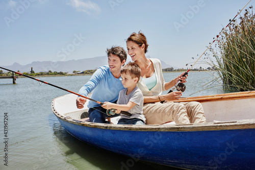 Parents with fishing rod sitting by son in rowboat on lake photo