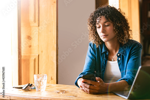 Young female freelancer using smart phone at home office photo