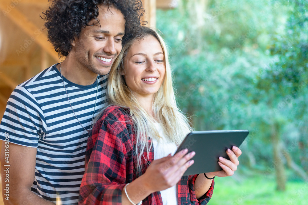 Young couple using digital tablet while standing by window at front yard Young couple using digital tablet while standing by window at front yard