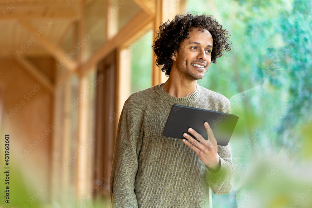 Young man with digital tablet looking away while standing by window Young man with digital tablet looking away while standing by window