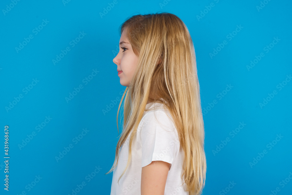 Profile portrait of nice beautiful Caucasian little girl wearing white T-shirt over blue background look empty space toothy smile Profile portrait of nice beautiful Caucasian little girl wearing white T-shirt over blue background look empty space toothy smile