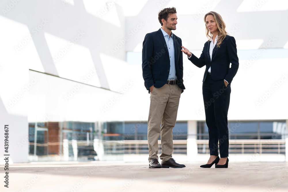 Businesswoman talking with colleague while standing at office building terrace Businesswoman talking with colleague while standing at office building terrace