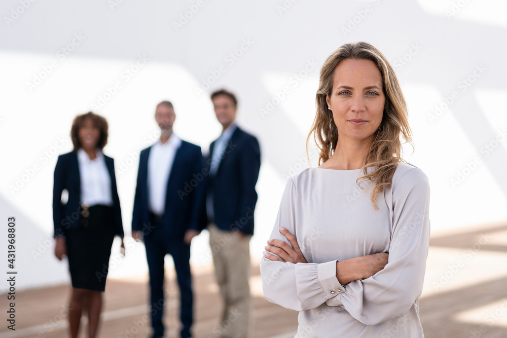 Confident businesswoman staring while standing with colleagues in background at office terrace Confident businesswoman staring while standing with colleagues in background at office terrace