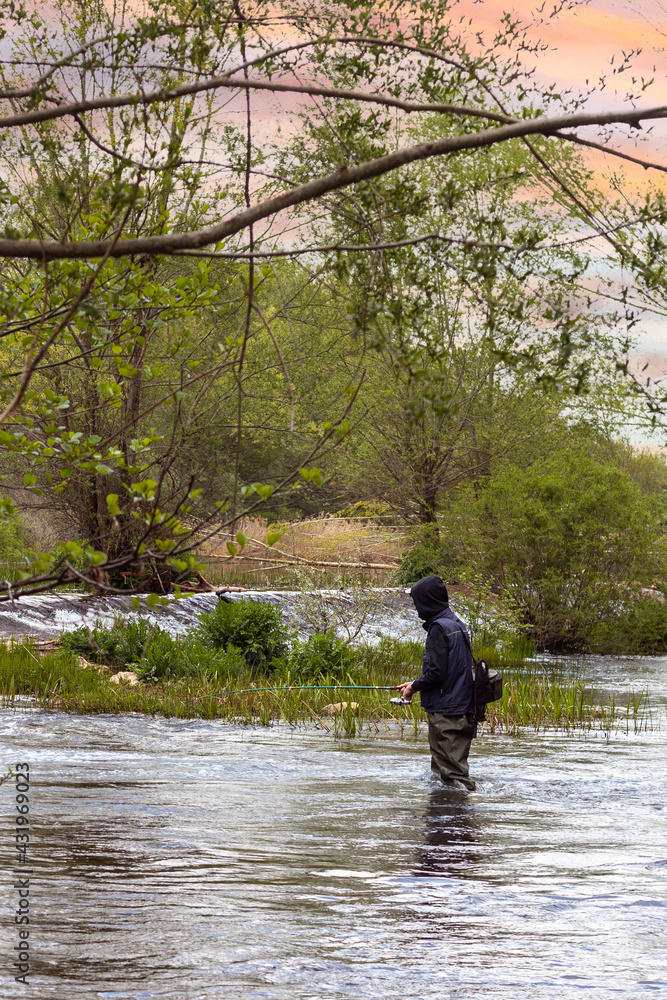 Selective focus of a young man fishing in the middle of a river with long rubber fishing boots Selective focus of a young man fishing in the middle of a river with long rubber fishing boots