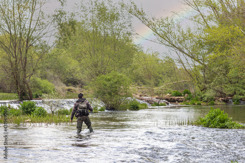 Canvas-taulu Boy fishing in the middle of a river with rocks, weeds and bushes with camouflag