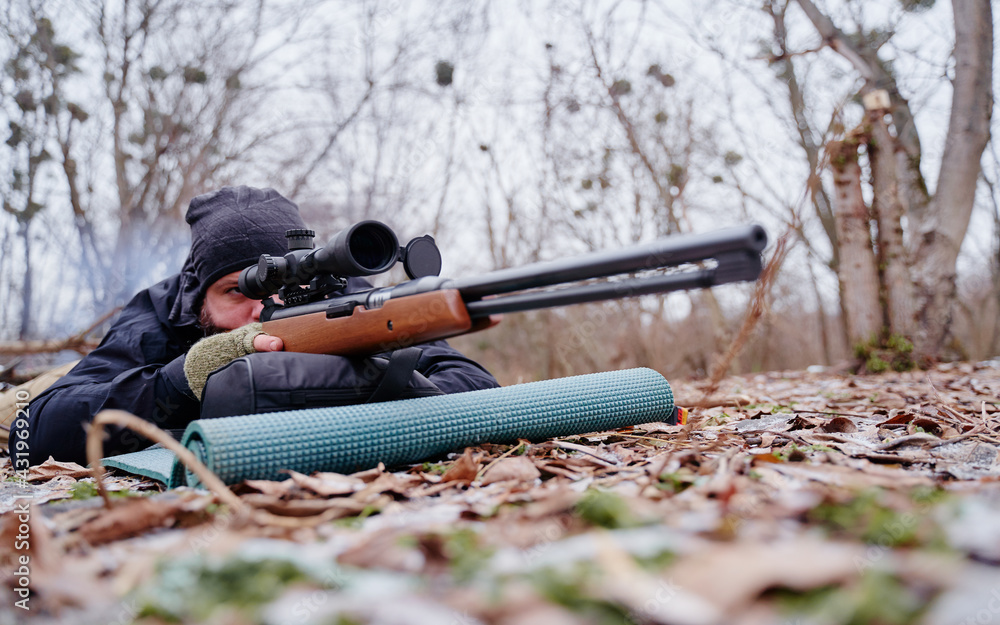 Young man aiming at target with the hunting rifle.